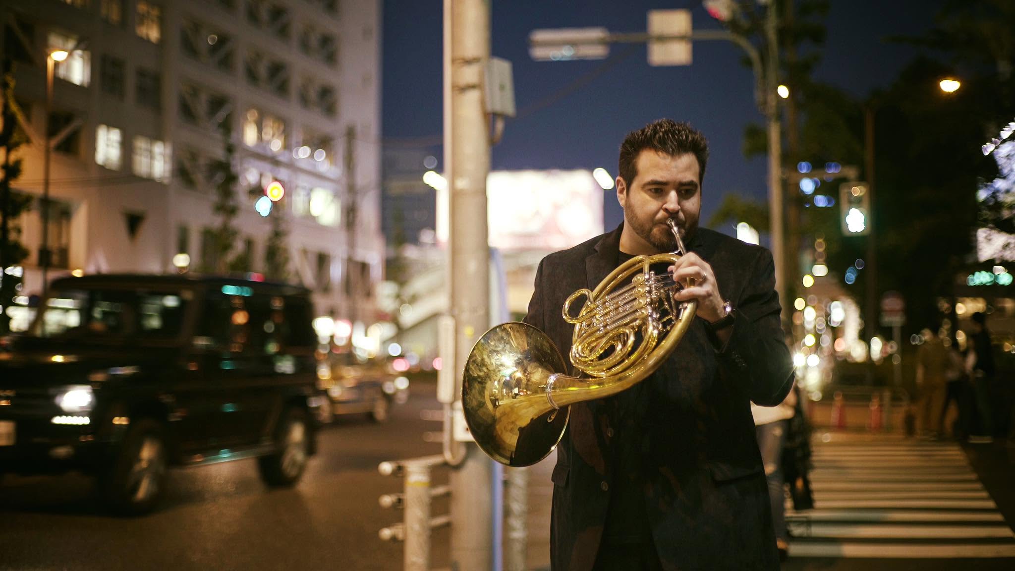 Chris Castellanos playing horn on a city street at night